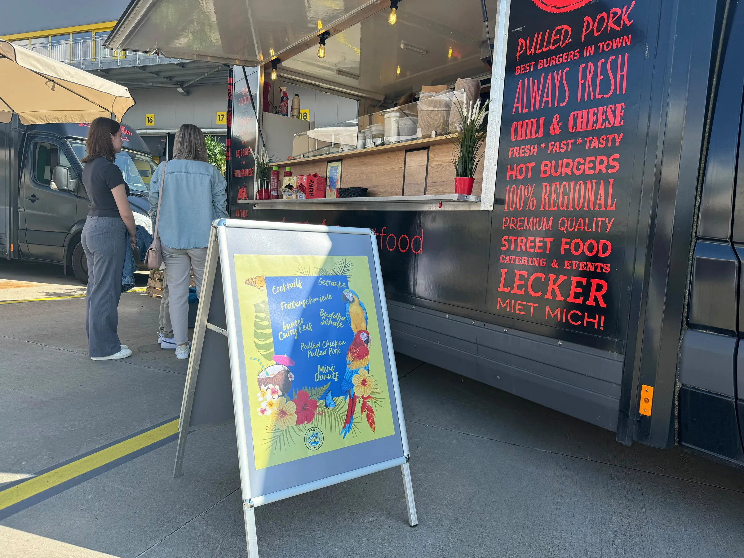 Gäste stehen bei Tageslicht am La Tapita Foodtruck mit Menütafel an
